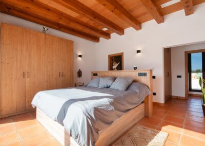 Dormitorio con cama de matrimonio, un gran armario de madera y techo con vigas.