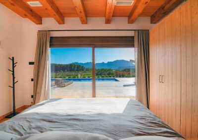 Dormitorio con grandes puertas de cristal y vistas al jardín, la piscina y las montañas