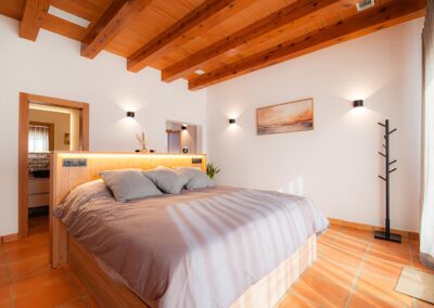 Amplio dormitorio con cama de matrimonio, un cuadro moderno y techo con vigas de madera.
