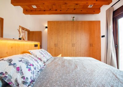 Primer plano de dormitorio con cama de matrimonio, un gran armario de madera y techo con viga