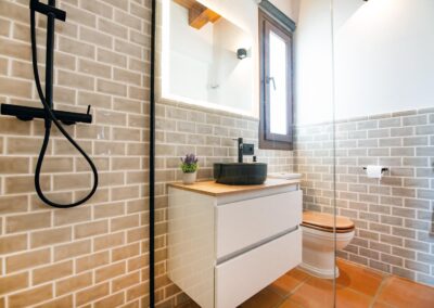 Cuarto de baño moderno con un lavabo negro, inodoro, paredes de azulejos y suelo de terracota