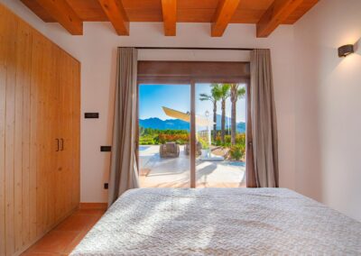 Dormitorio con armario de madera y grandes puertas de cristal con vistas a una terraza y a las montañas