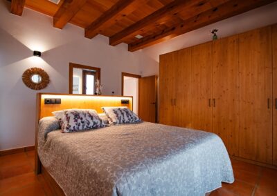 Dormitorio con cama de matrimonio, un gran armario de madera y techo con vigas.