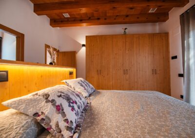 Primer plano de una cama con un cabecero de madera iluminado y un closet de madera moderno.