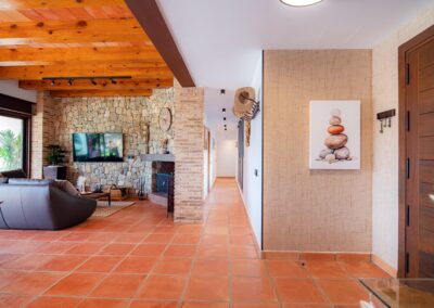 Pasillo de una casa con suelo de terracota, que se abre a un salón con una pared de piedra