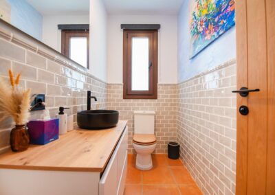 Baño con paredes de azulejo y un moderno mueble de lavabo suspendido con encimera de madera y lavabo negro.