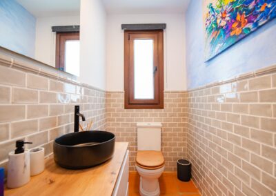 seo con azulejos, un lavabo negro sobre un mueble de madera y suelo de terracota. Un cuadro de colores vivos decora la pared.