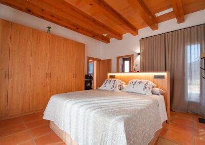 Amplia habitación de estilo rústico con un gran armario de pino, una cama con cabecero iluminado y un techo de vigas de madera a juego