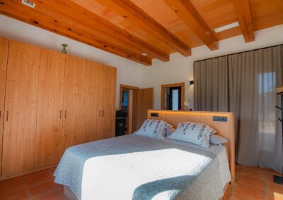 Dormitorio con cama de matrimonio, un gran armario de madera y techo con viga