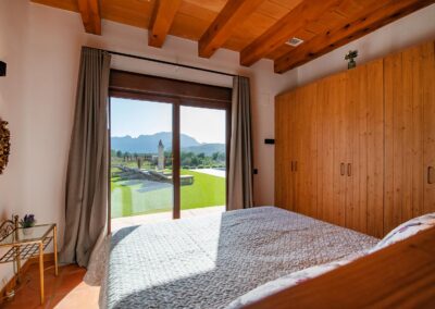 Dormitorio con grandes puertas de cristal y vistas al jardín, la piscina y las montañas