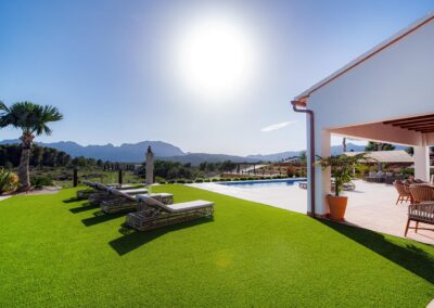Jardín de una villa con tumbonas sobre el césped y vistas a las montañas.