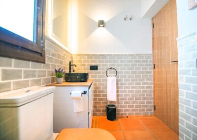Cuarto de baño moderno con un lavabo negro, azulejos grises y suelo de terracota.