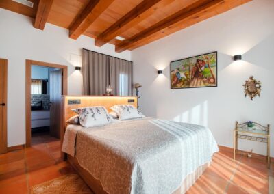 Dormitorio con cama de matrimonio, techo con vigas de madera y acceso a un cuarto de baño