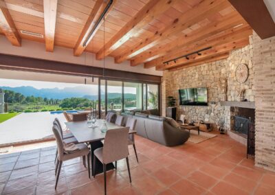 Vista desde el comedor, a través de grandes puertas de cristal abiertas, hacia una terraza con piscina y una espectacular vista de las montañas