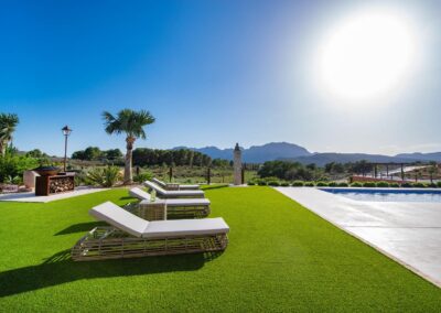 Zona para tomar el sol con tumbonas de diseño sobre un césped verde, con vistas a un paisaje de montañas y una torre de piedra a lo lejos