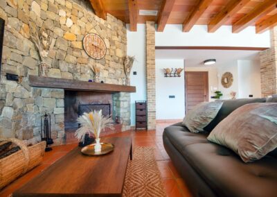 Salón rústico con una gran chimenea de piedra, sofá y techo con vigas de madera