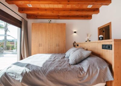 Habitación de estilo rústico con un gran armario de pino a la derecha de la cama. El cabecero de la cama tiene una luz integrada y el techo es de vigas de madera.