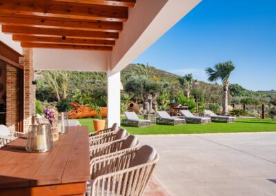 Terraza cubierta con una mesa de comedor que da a un jardín con césped y tumbonas